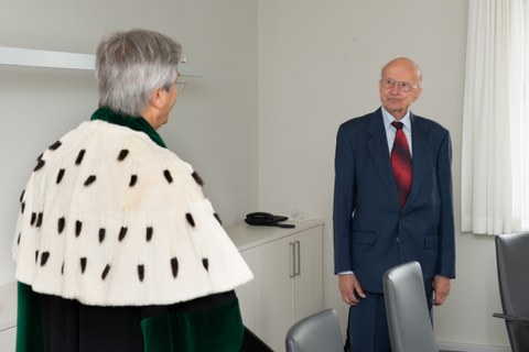 Links ist Rektor Müller-Steinhagen von hinten zu sehen. Mit Gesicht in die Kamera gewand, Prof. Winfried Hacker aufrecht stehend.