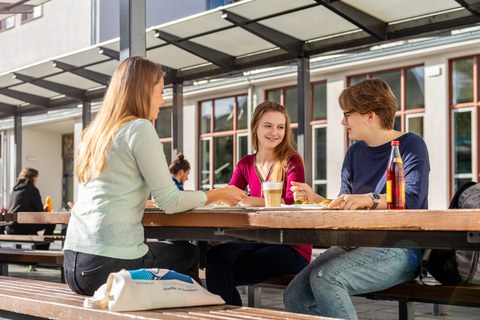 Studierende sitzen im Außenbereich der Mensa