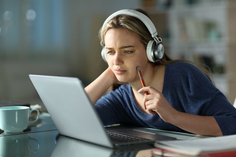 Das Foto zeigt eine junge Frau an einem Tisch. Sie schaut nachdenklich auf ihren Laptop.