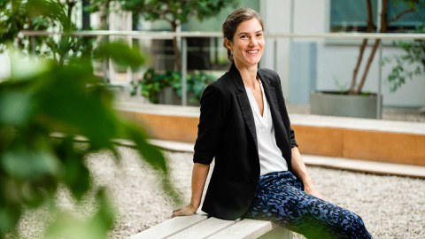 Elena Hassinger sitzt im freien auf einer Bank. Vor ihr sind unscharf einige Blätter.