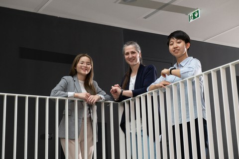 Foto von zwei taiwanesischen und einem deutschen Studierenden, die im Hermann-Krone-Bau an einer weißen Balustrade stehen und in die Kamera lächeln.