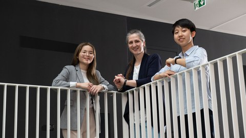 Foto von zwei taiwanesischen und einem deutschen Studierenden, die im Hermann-Krone-Bau an einer weißen Balustrade stehen und in die Kamera lächeln.