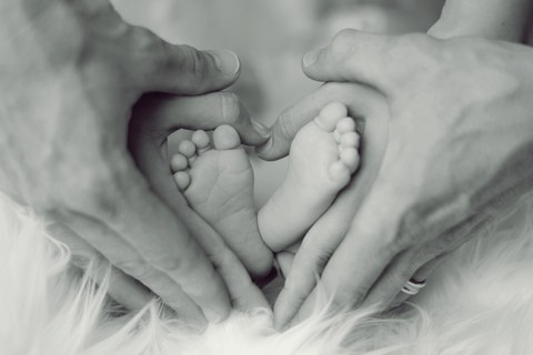 Füße eines Säuglings umrahmt von den Händen der Eltern.