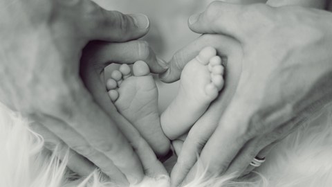 Füße eines Säuglings umrahmt von den Händen der Eltern.