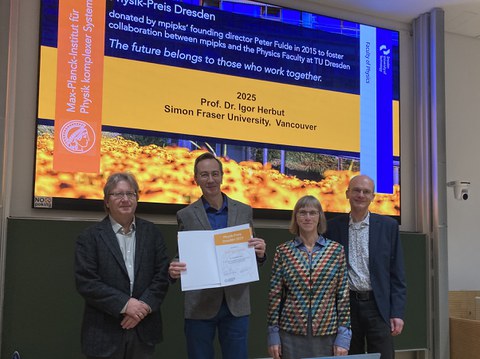 Vier Personen stehen auf dem Podium. Der Preisträger hält die Urkunde in den Händen.