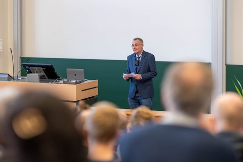 Ein Mann steht vor der Tagel und spricht ins Mikrofon.