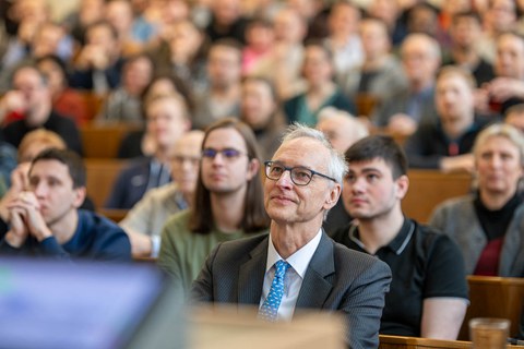 Hinter einem Mann sitzen viele Menschen im Hörsaal