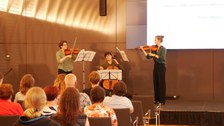 Drei Streicher spielen auf der Bühne. Zwei Geigen und ein Cello