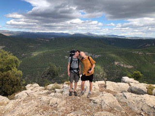 Zwei Männer mit Rucksack stehen auf einem Berg und schauen in die Kamera.