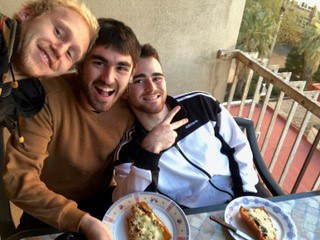 Drei Personen sitzen am Tisch und lachen in die Kamera.