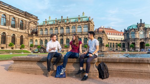 Drei TU Studenten sitzen an einem Springbrunnen im Dresdner Zwinger und unterhalten sich.