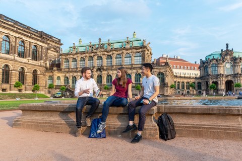 Drei TU Studenten sitzen an einem Springbrunnen im Dresdner Zwinger und unterhalten sich.