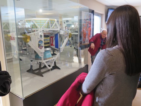 Eine junge Frau steht vor dem Modell des Antimateriedetektors, der an der Raumstation ISS angebracht ist.