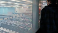 Vom Besucherraum des CERN Control Centre aus blickt ein Student durch eine Glaswand auf ein Meer von Prozessoren unterhalb des Raumes.