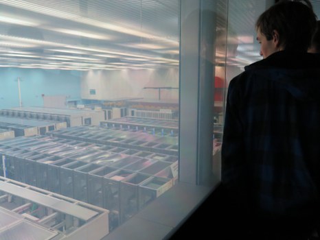 Vom Besucherraum des CERN Control Centre aus blickt ein Student durch eine Glaswand auf ein Meer von Prozessoren unterhalb des Raumes.
