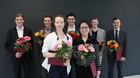 Gruppenaufnahme der sieben Preisträger:innen mit jeweils einem Blumenstrauß in der Hand
