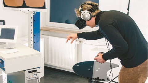 Ein Mann testet zwischen Monitoren und anderen Geräten, mit Kopfhörern und VR-Brille, die Virtual Reality aus.