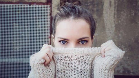 Eine junge Frau versteckt ein Lächeln unter einem dicken Pullover.