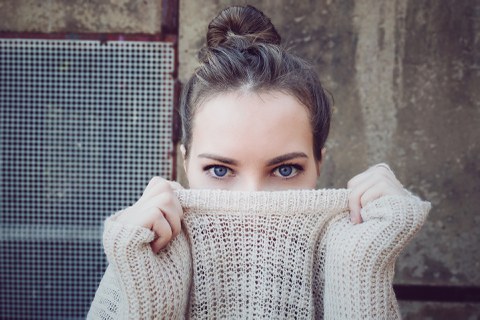 Eine junge Frau versteckt ein Lächeln unter einem dicken Pullover.