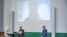 Zwei Professoren stehen vorn im Hörsaal. An der Wand ist eine Videoschalte projeziert.