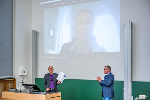 Zwei Professoren stehen vorn im Hörsaal. An der Wand ist eine Videoschalte projeziert.