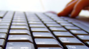 Das Foto zeigt eine Nahaufnahme einer Laptoptastatur, sowie die Hand einer Person, welche den Laptop bedient.
