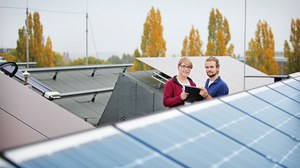 Das Foto zeigt zwei Studierende auf einem Dach mit Solaranlagen. Beide halten gemeinsam ein Clipboard in den Händen.