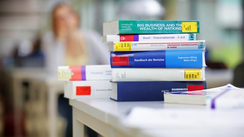  Das Foto zeigt eine Stapel Bücher aus der Bibliothek zum Thema Handel und Finanzen. Sie liegen übereinander auf einem Tisch. 