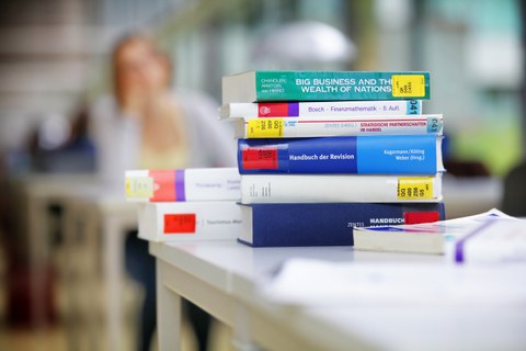  Das Foto zeigt eine Stapel Bücher aus der Bibliothek zum Thema Handel und Finanzen. Sie liegen übereinander auf einem Tisch. 