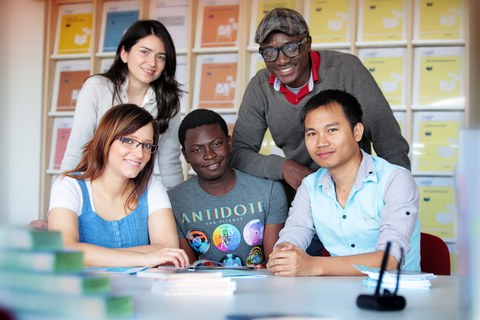  Das Foto zeigt fünf Personen. Sie sitzen bzw. stehen an einem Tisch und lächeln in die Kamera. Auf dem Tisch liegen einige Bücher.