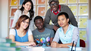  Das Foto zeigt fünf Personen. Sie sitzen bzw. stehen an einem Tisch und lächeln in die Kamera. Auf dem Tisch liegen einige Bücher.