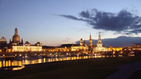 Das Foto zeigt die dresdner Skyline von der Frauenkirche bis zur Semperoper bei Abenddämmerung. In der Elbe spiegeln sich die Lichter der Stadt.