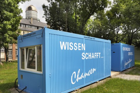 Das Foto zeigt  zwei blaue Container mit der Aufschrift "Wissen schafft... Chancen" und "Knowledge creates... fascination", welche auf einer Wiese des Campus der TU Dresden stehen.