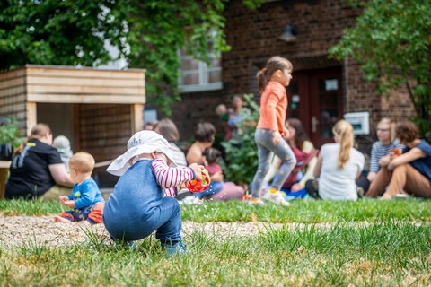 Foto: Eltern sitzen und spielen mit ihren Kindern auf dem Spielplatz des Kindergarten "Campusnest"