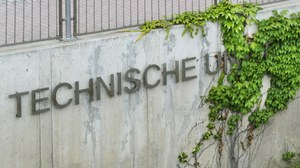 Das Foto zeigt eine Mauer an welcher der Schriftzug " Technische Universität" angebracht ist. Das Wort "Universität" ist von Efeu überwachsen.