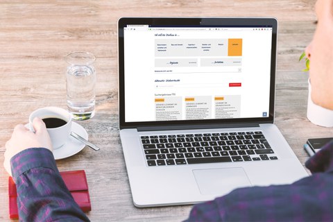 Das Foto zeigt eine Person, welche an einem Laptop sitzt, auf dessen Bildschirm die Webseite des Studieninformationssystems der TU Dresden geöffnet ist. Neben dem Laptop befinden sich ein Wasserglas und eine Kaffeetasse.