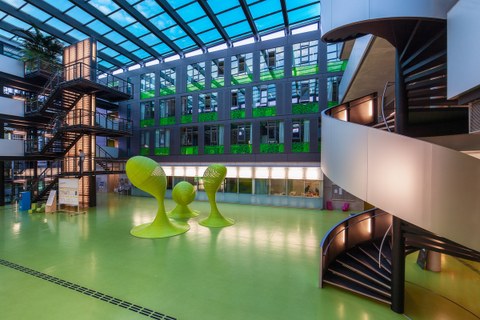 Das Foto zeigt das Foyer des Andreas-Pfitzmann-Baus der TU Dresden. Der Boden des Foyers ist grün. In der Mitte stehen drei grüne Skulpturen. 