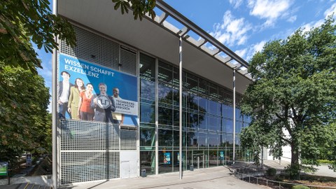 Frontansicht des Hörsaalzentrums der TU Dresden. Am Gebäude Hängt ein Poster mit der Aufschrift: "Wissen Schafft Exzellenz".