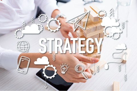 Foto von Frauenhänden, die einen Turm aus Holzsteinen bauen. Darüber liegt eine transparente Illustration mit verschiedenen Symbolen und der Aufschrift "Strategy".