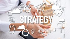 Foto von Frauenhänden, die einen Turm aus Holzsteinen bauen. Darüber liegt eine transparente Illustration mit verschiedenen Symbolen und der Aufschrift "Strategy".