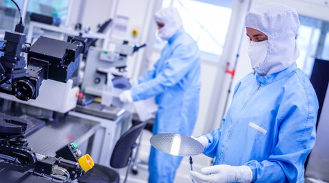 Photo of people in protective clothing in a laboratory. One person is holding a silicon wafer. 