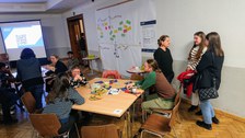 Foto von Diskussionsrunde von Teilnehmer:innen mit Flipchart mit bunten Zetteln im Hintergrund