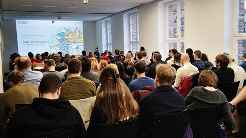 voller Saal mit Studierenden - PowerPoint Präsentation mit "Karriere mit Geist" und buntem Bild an die Wand gestrahlt