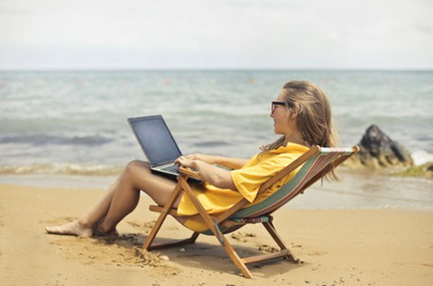 Frau im Liegestuhl am Strand mit Laptop