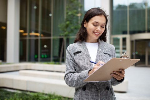 Smiling businesswoman reading documents and signing papers on clipboard outside