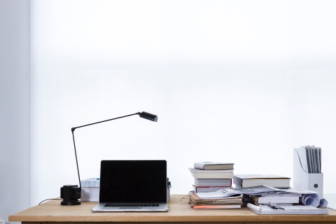 desk with laptop, lamp, books, sheets of paper and workbooks