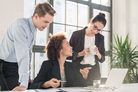 Drei Personen diskutieren am Schreibtisch vor einem Laptop