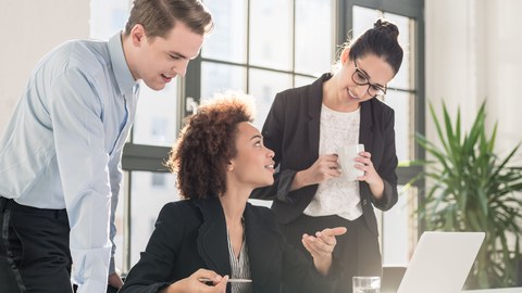 Three persons discuss in front of a computer.