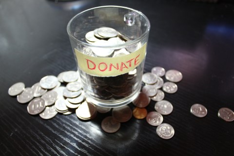 Jar with label "donate". A lot of coins in the jar and some coins on the table around the jar.