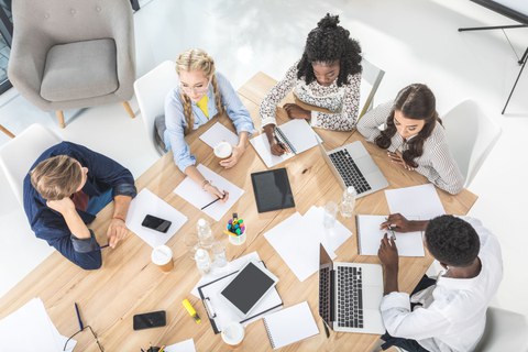 Mitarbeiter sitzen mit Laptops und schriftlichen Notizen um Tisch und planen